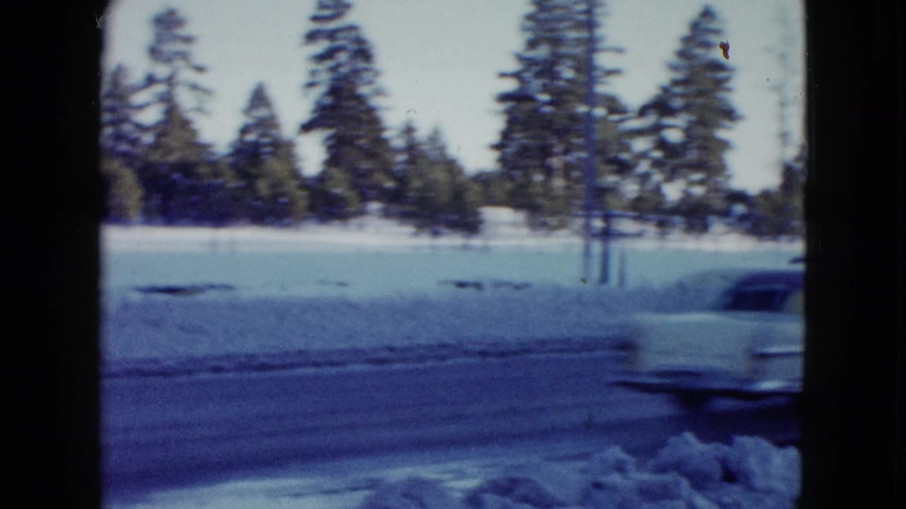 A light-colored car passes through a snowy Las Vegas-area roadside view, framed by 8mm film edges and winter trees.