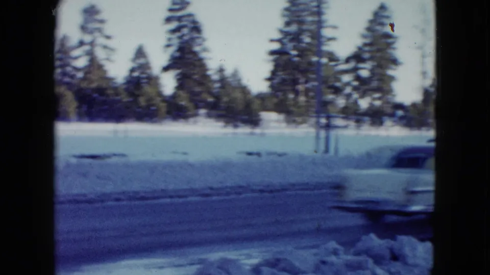 A light-colored car passes through a snowy Las Vegas-area roadside view, framed by 8mm film edges and winter trees.