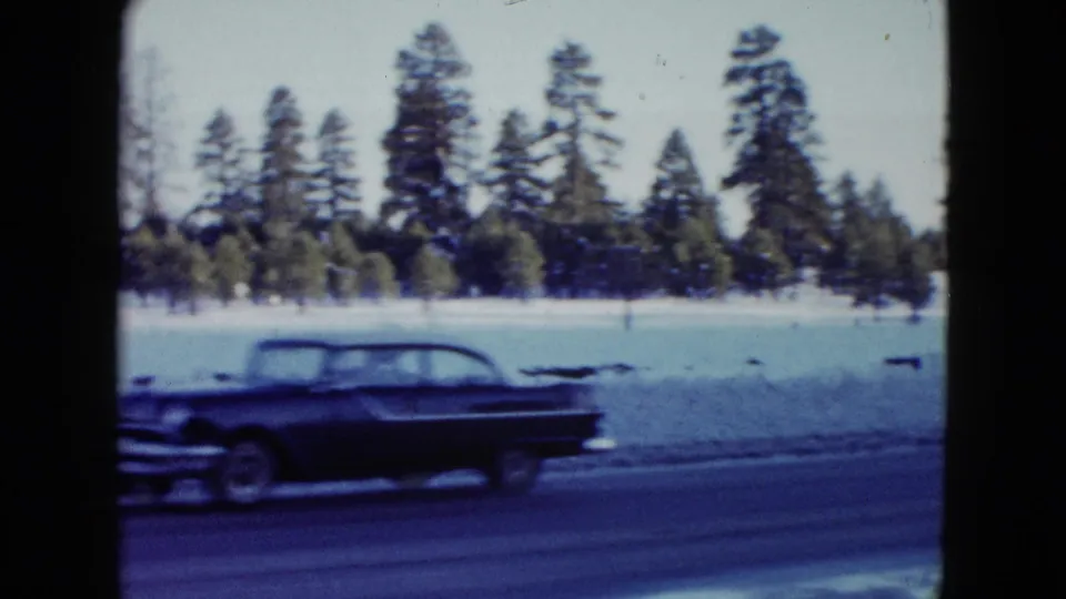 A dark 1950s-style automobile moves along a snowy highway in the 1958 Las Vegas-area home-movie footage.