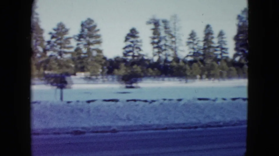 Snowbanks and tall trees line the roadside in this 1958 Las Vegas-area 8mm frame after traffic has passed.