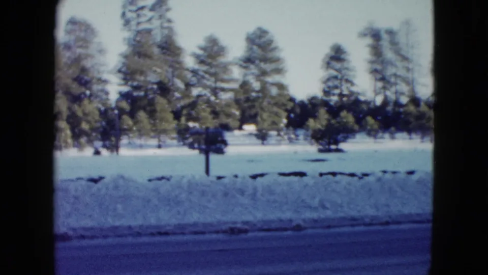 1958 8mm home-movie frame of a snow-covered rural roadside near Las Vegas, with evergreen trees beyond the road.