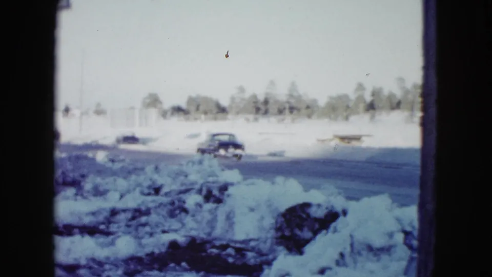 A dark car continues along a snowbound rural road near Las Vegas, recorded on soft, blue-shifted 8mm film in 1958.