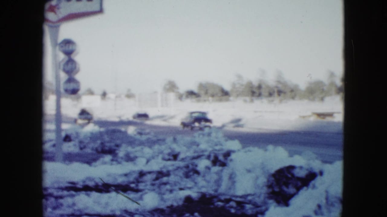1958 Las Vegas snowy roadside viewed from inside a vehicle, with classic cars and a partially visible Mobil station sign.