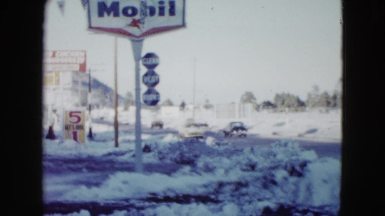 Snowy Las Vegas street in 1958 with a visible Mobil sign, roadside buildings, and classic cars moving through the frame.