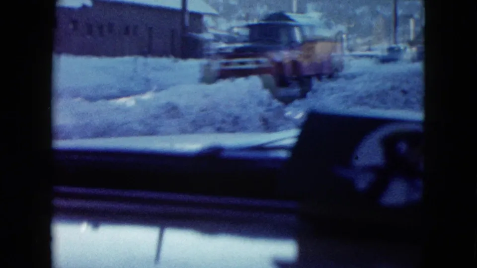 A work truck or snowplow passes along a snowy Las Vegas street, framed by the dashboard and windshield of the filming vehicle.