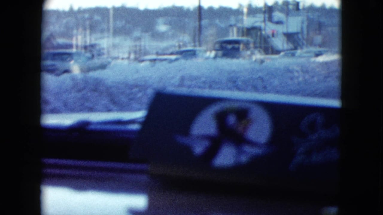 Snowy street seen through a car windshield with dashboard and air freshener in the foreground.