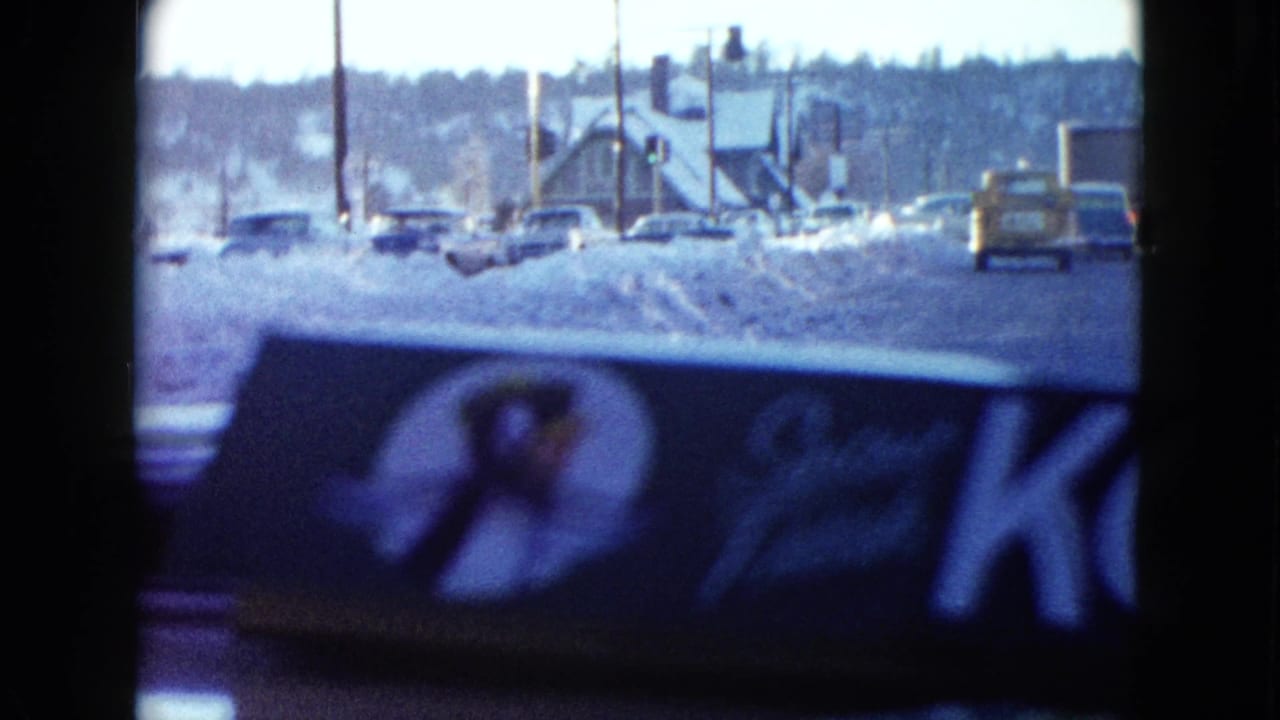 Car-window view of a snowy Las Vegas roadside with parked vehicles, poles, buildings, and a branded dashboard air freshener.