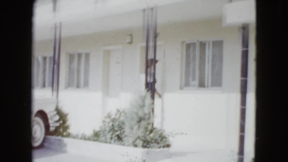 Mid-century house exterior in Las Vegas with porch posts, windows, shrubs, and a partial car visible at frame edge.