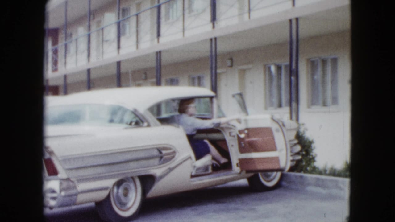 In 1958 Las Vegas footage, a woman sits by the open door of a white finned car parked outside a two-story motel.