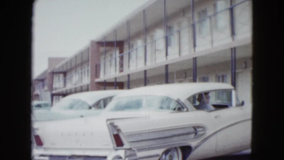 A white 1950s automobile fills the foreground outside a Las Vegas motel, with more parked cars along the lot.