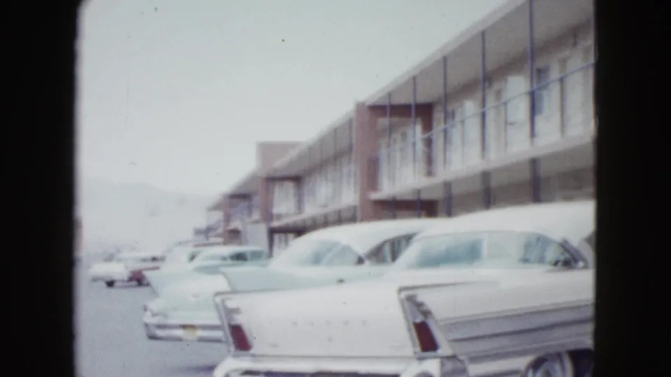 Rear view of a white finned car in a Las Vegas motel parking lot, with exterior corridors and other cars in view.