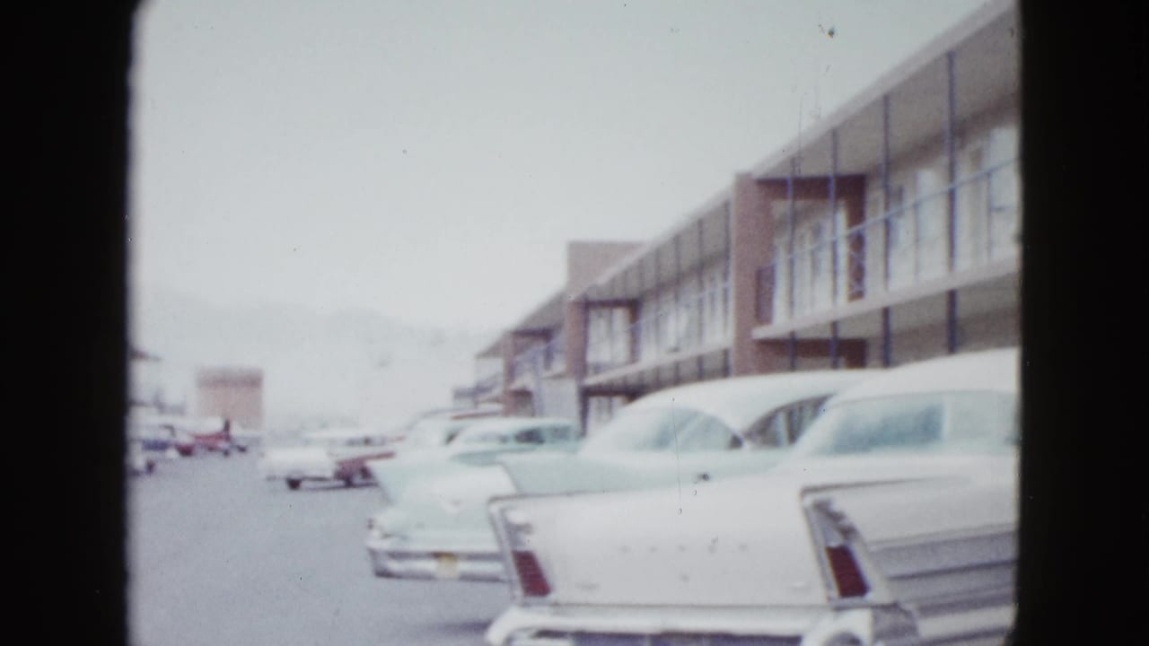 Two-story motel exterior with parked 1950s cars and dark 8mm frame edges.