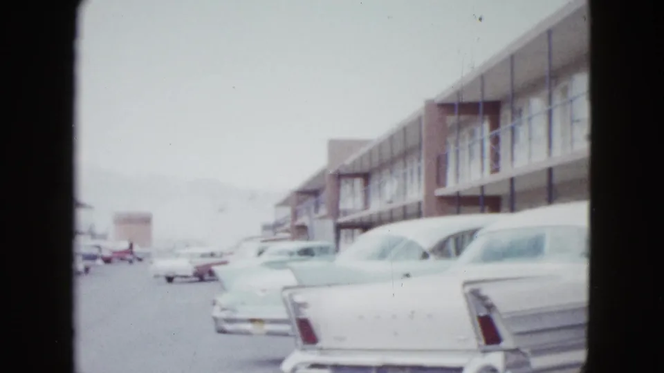 1958 Las Vegas home-movie frame showing a motel parking area, balcony-front rooms, and chrome-trimmed cars.