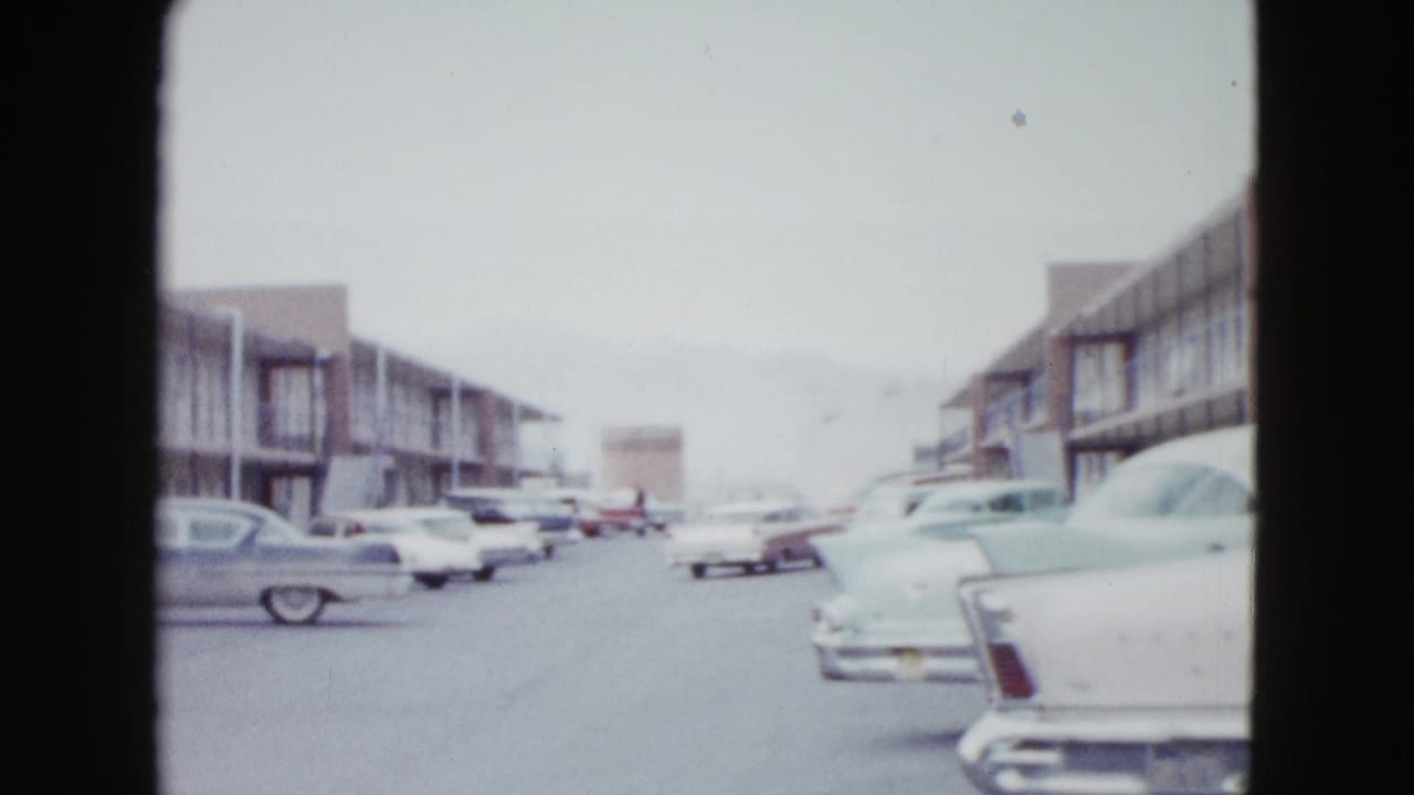 Las Vegas motel exterior with multiple 1950s automobiles parked along two-story lodging buildings.