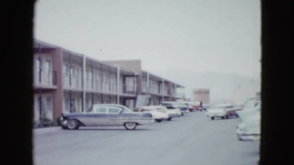 1958 Las Vegas frame showing a motel row, parked finned cars, and a broad paved lot in faded 8mm color.