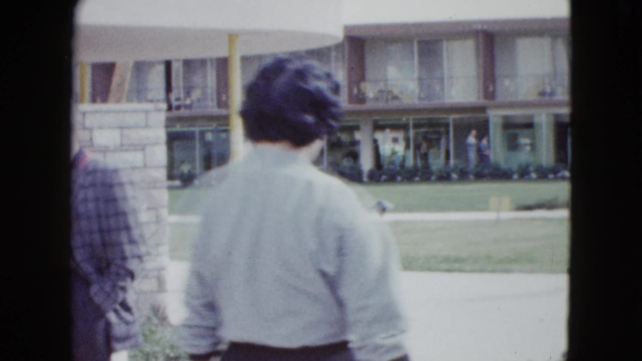 Adults walking away from the camera toward a two-story motel building with lawn and windows.