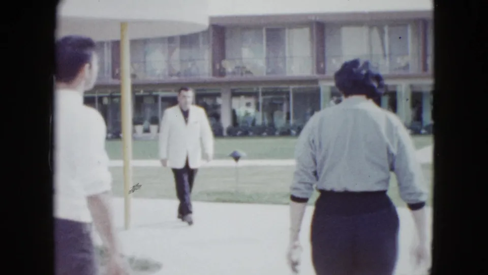 A man in a light jacket approaches while other adults pass through a Las Vegas motel courtyard in this 1958 home-movie frame.