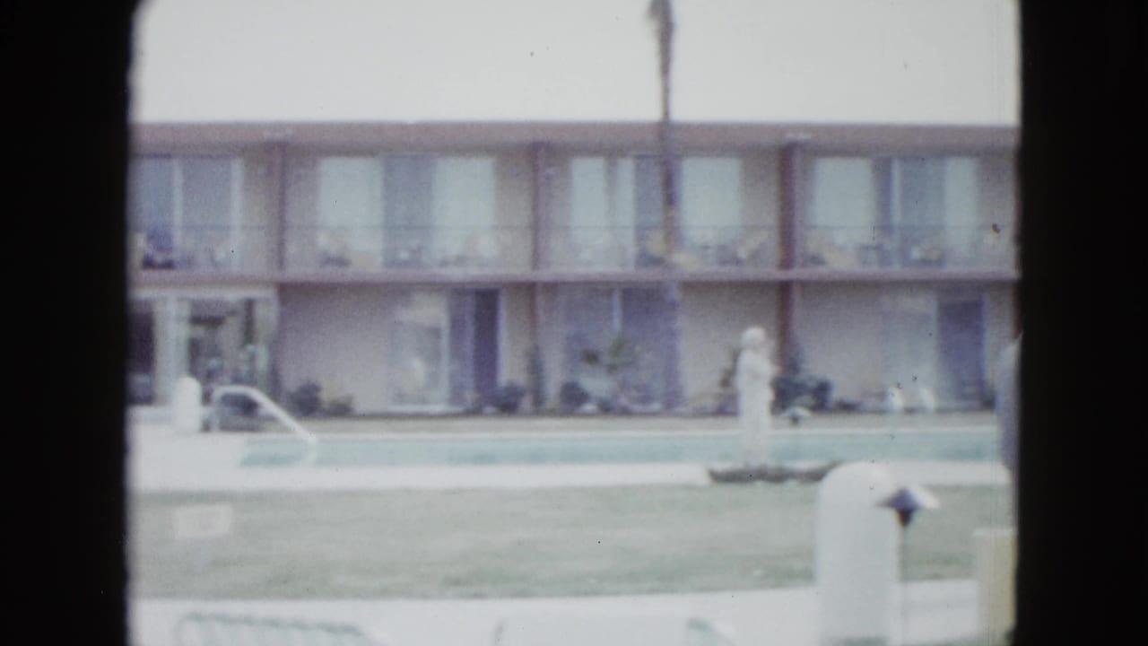 1958 Las Vegas motel poolside view with a two-story room block, lawn, pool edge, and an adult woman in white near the water.