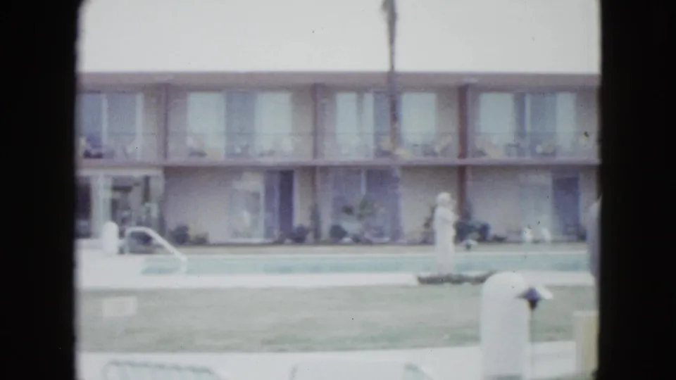 1958 Las Vegas motel poolside view with a two-story room block, lawn, pool edge, and an adult woman in white near the water.