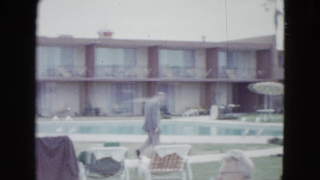 Las Vegas motel pool area with a walking man, striped umbrella, lounge chair, lawn, and two-story rooms in soft 8mm color.