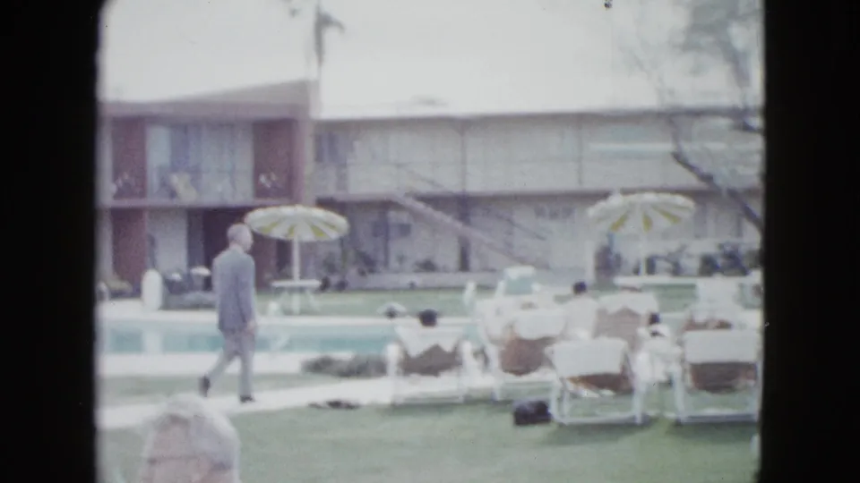 1958 Las Vegas hotel common area with pool loungers, striped umbrellas, lawn, and a man walking near two-story motel buildings.