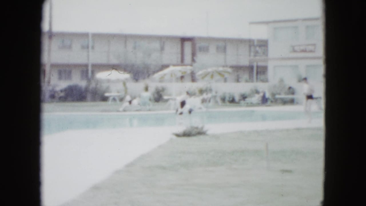 Las Vegas resort pool in 1958, with guests near a long pool, striped umbrellas, lounge seating, palm trees, and a motel facade behind them.