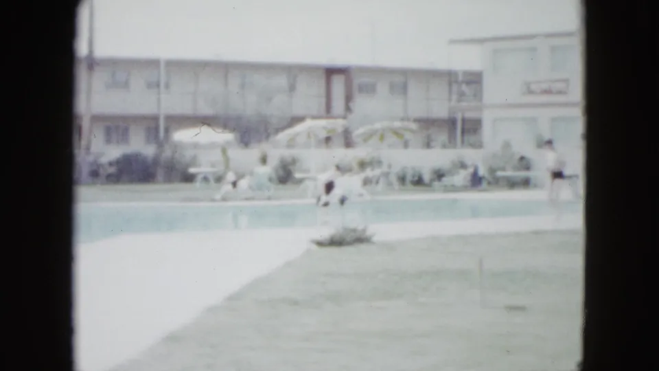 Las Vegas resort pool in 1958, with guests near a long pool, striped umbrellas, lounge seating, palm trees, and a motel facade behind them.