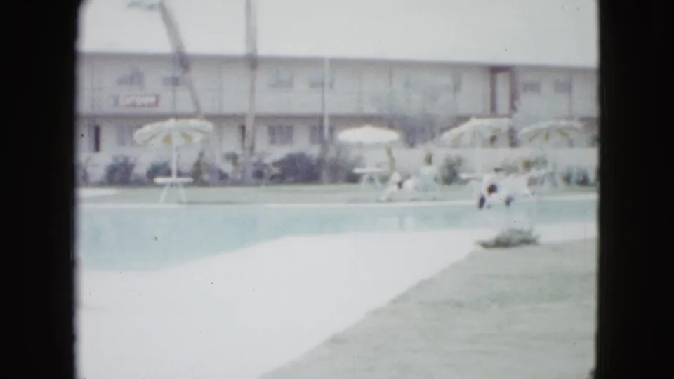 Mid-century Las Vegas motel pool scene with striped umbrellas, lawn, palm trunks, and guests relaxing or walking beside the water.