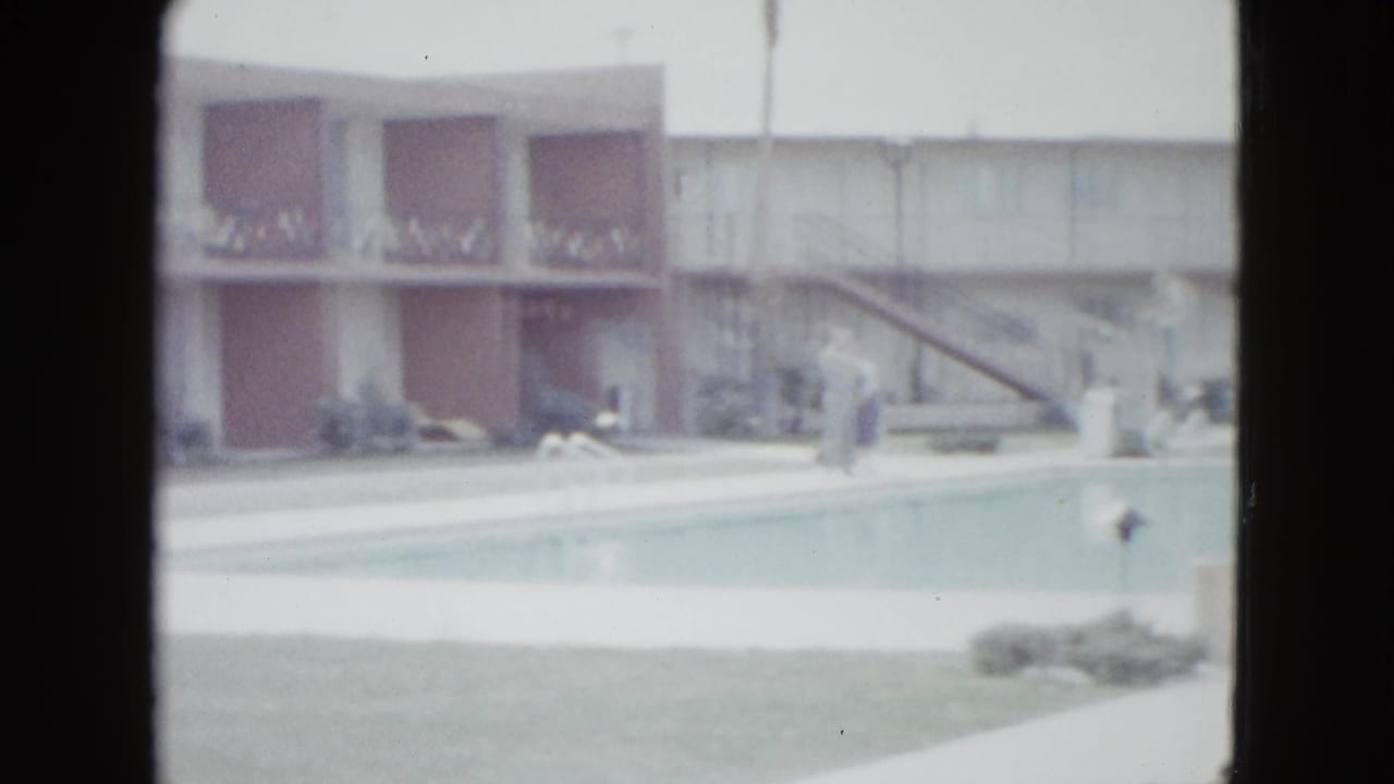 Las Vegas motel pool scene from 1958 with balcony railings, reddish-brown wall panels, deck furniture, umbrella, and indistinct people.