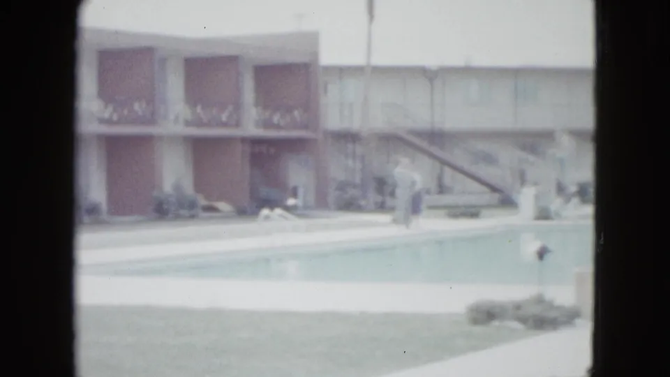 Las Vegas motel pool scene from 1958 with balcony railings, reddish-brown wall panels, deck furniture, umbrella, and indistinct people.