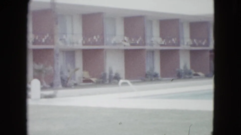 1958 Las Vegas motel courtyard view with pool water, white coping, lawn, shrubs, and a two-story building with repeated balcony bays.