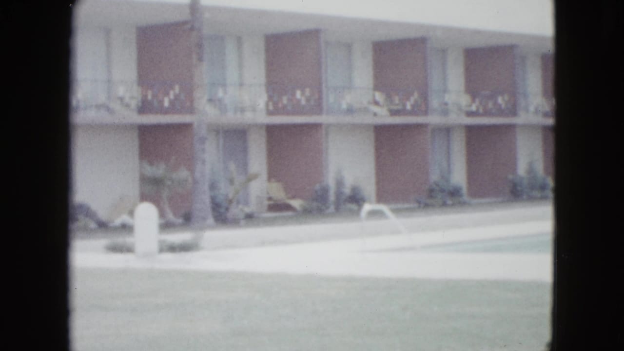 1958 Las Vegas hotel or motel exterior with balconies, lawn, and parking area in soft 8mm footage.