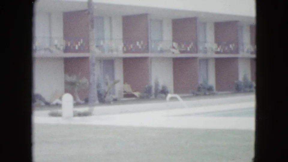 1958 Las Vegas hotel or motel exterior with balconies, lawn, and parking area in soft 8mm footage.