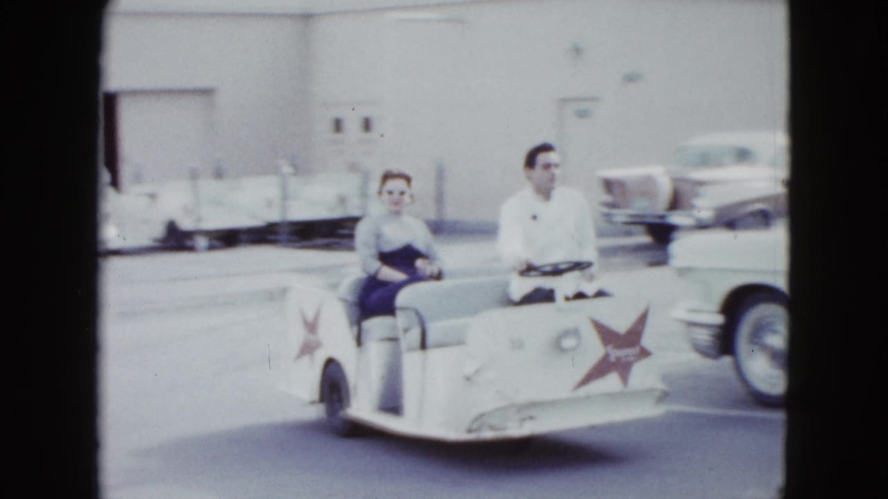 A woman passenger and male driver ride a white shuttle cart through a Las Vegas hotel parking area in 1958.