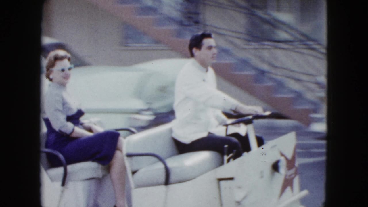 Close 8mm view of a dressed couple riding a white hotel shuttle cart in a Las Vegas parking area.