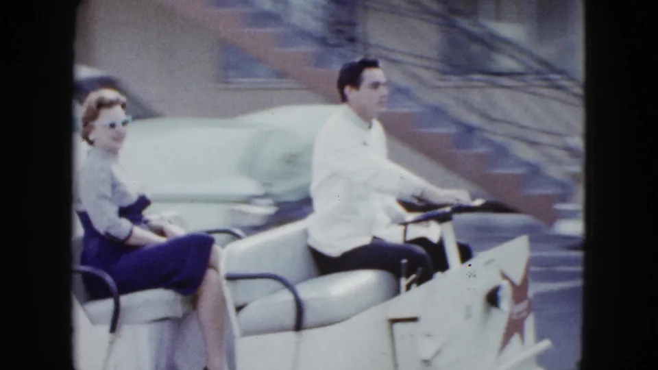Close 8mm view of a dressed couple riding a white hotel shuttle cart in a Las Vegas parking area.
