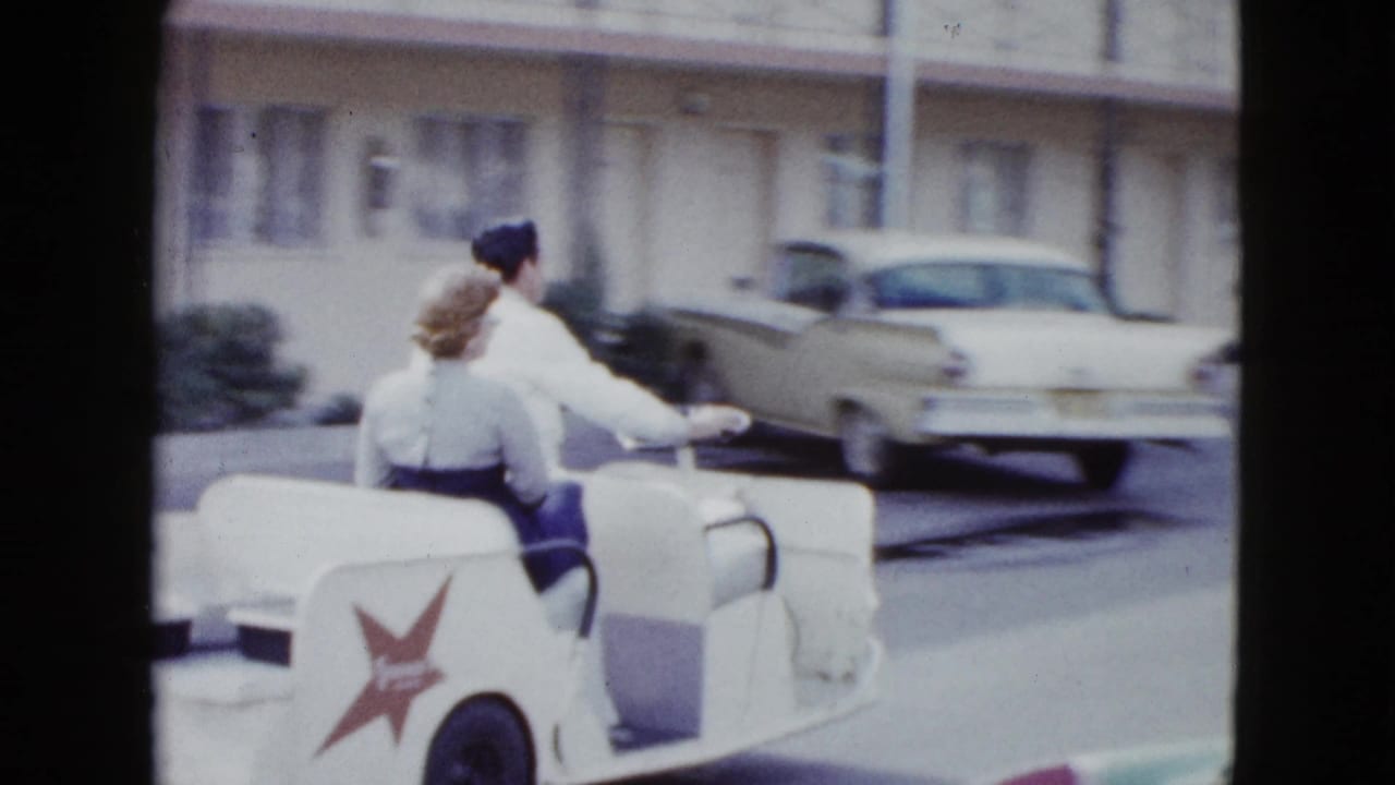 The couple continues through a Las Vegas motel driveway in a white open mini car with a red star logo on its side.