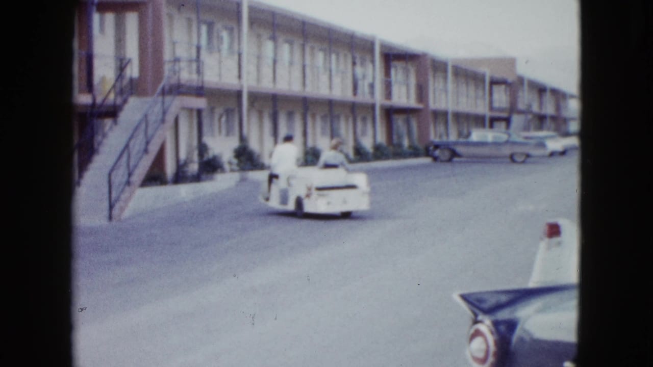The couple drives farther away through the Las Vegas motel complex, with exterior stairs, motel rooms, and period cars visible.