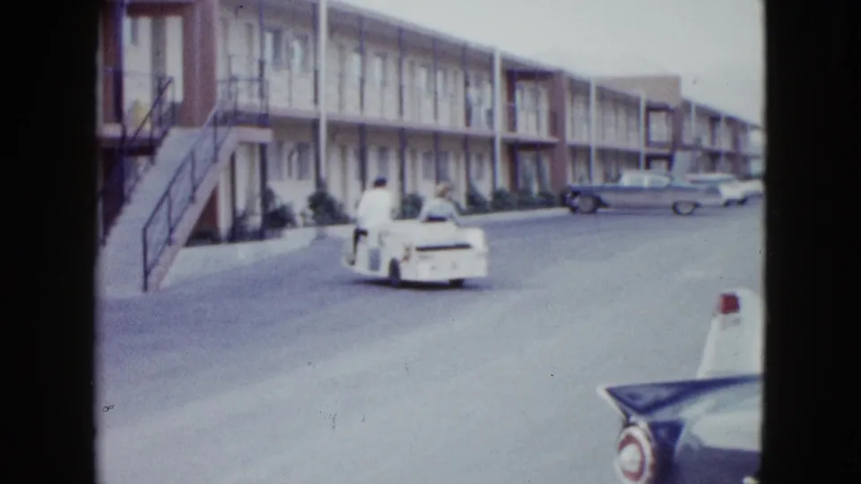 The couple drives farther away through the Las Vegas motel complex, with exterior stairs, motel rooms, and period cars visible.