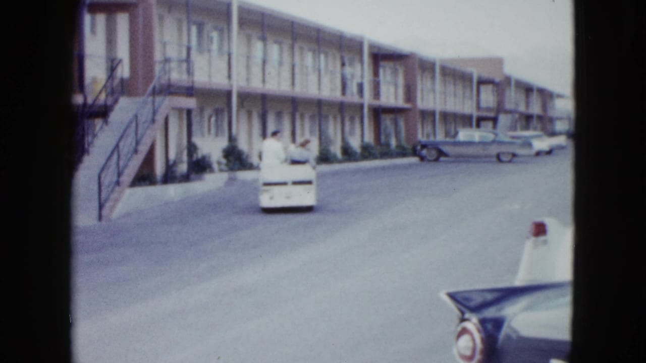 1958 Las Vegas home-movie frame showing a small white utility cart in front of a two-story motel and parked mid-century cars.
