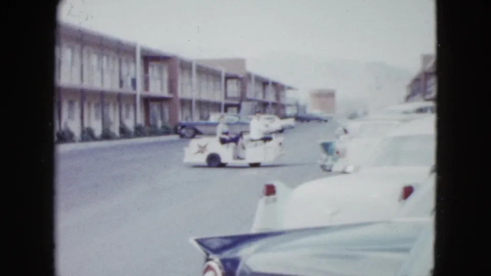 Home-movie frame from 1958 Las Vegas showing a cart with riders beside a motel row and parked 1950s cars.