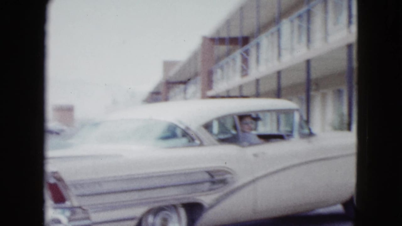 White 1950s sedan parked close to a two-story motel exterior.
