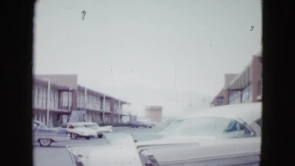 The view looks across a Las Vegas motel parking lot toward rows of parked cars and low two-story motel buildings.