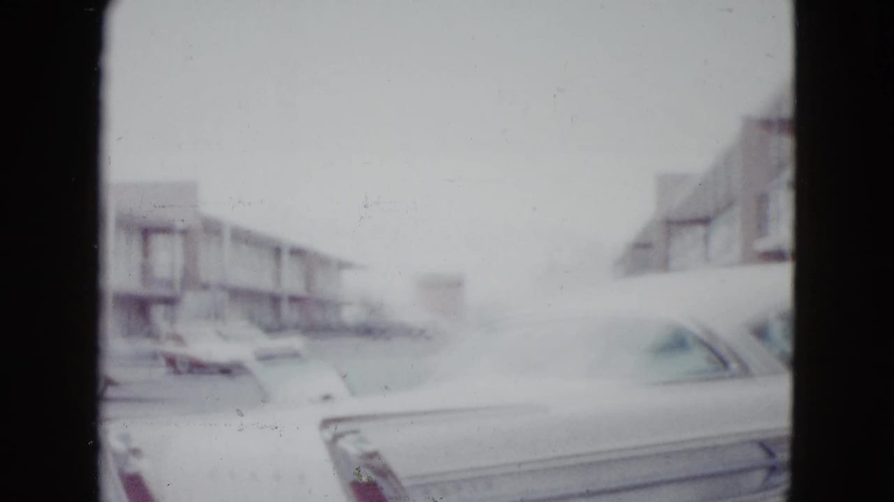 1958 Las Vegas home-movie frame showing a mid-century motel area with a classic car partly visible in the foreground.