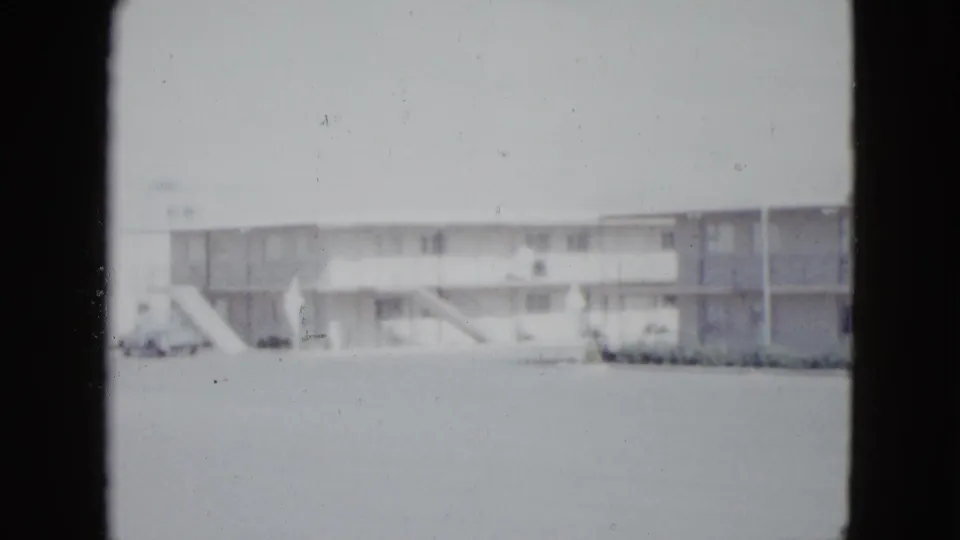 1958 Las Vegas frame of a long motel facade with exterior stairs, balcony railings, parked cars, and pale 8mm exposure.