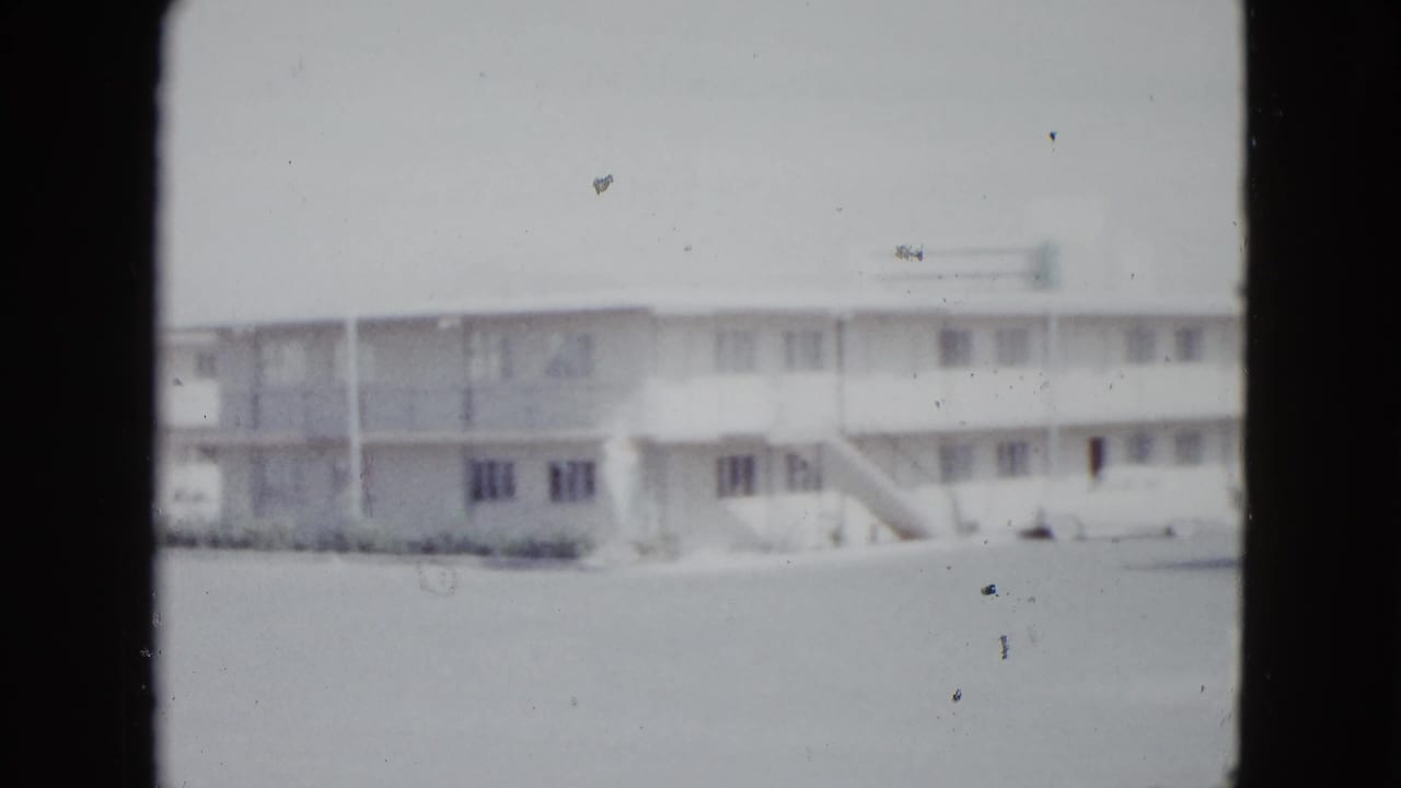 Soft 8mm frame of a two-story motel exterior seen across a parking area.