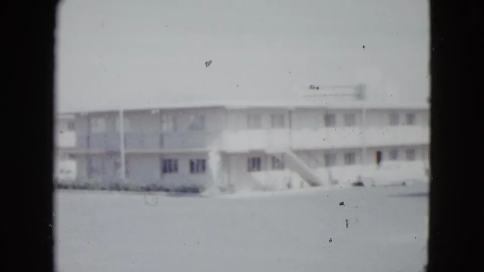 1958 Las Vegas home-movie frame showing a two-story motel-style building with exterior walkway, stairs, windows, and pale sky.