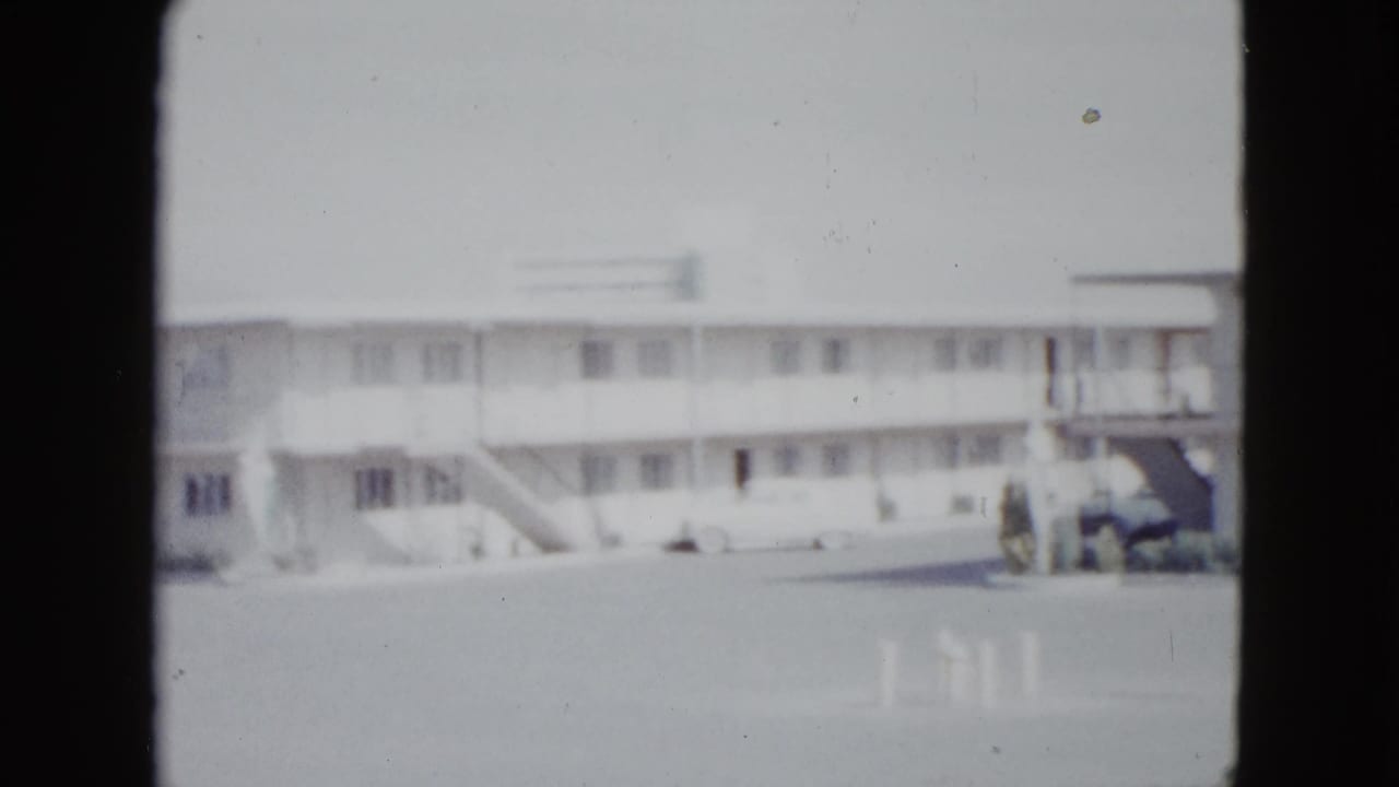 Motel facade with balcony railings, stairs, and a parked light-colored car at right.