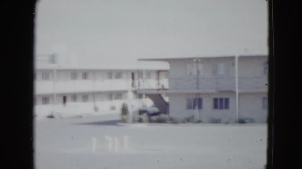 1958 Las Vegas frame showing the motel corner, exterior stairway, second-floor walkway, windows, and a light-colored parked car.