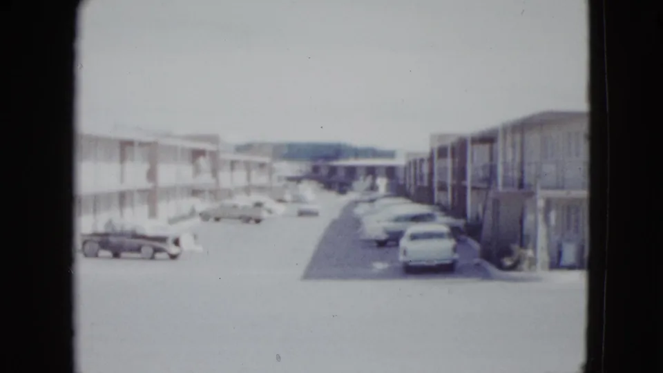 1958 Las Vegas home-movie view down a motel parking aisle, with two-story lodging blocks, exterior walkways, and parked cars.